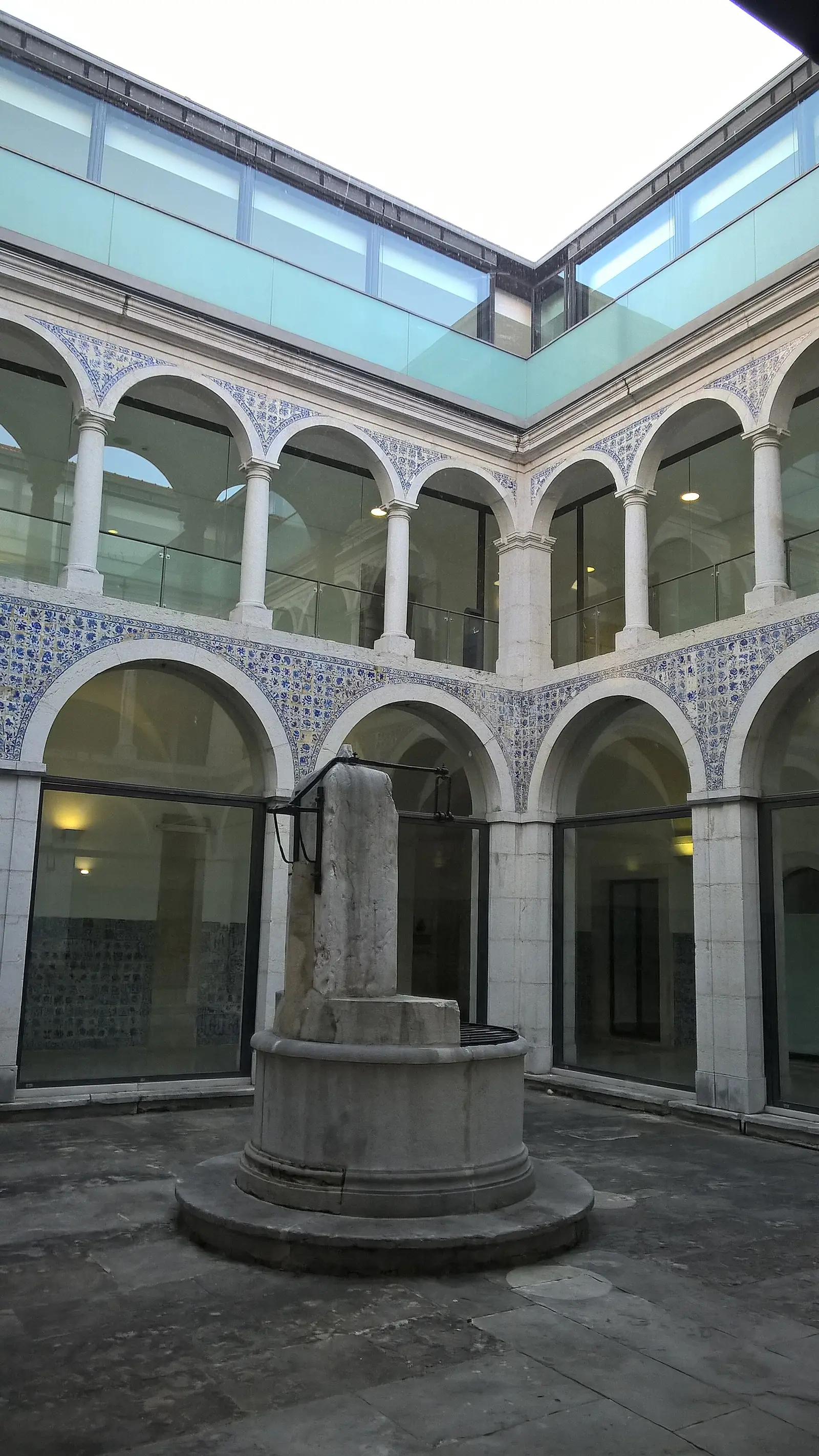 Pátio interior com arcadas brancas em dois andares, paredes forradas de azulejos e uma claraboia de vidro por cima.