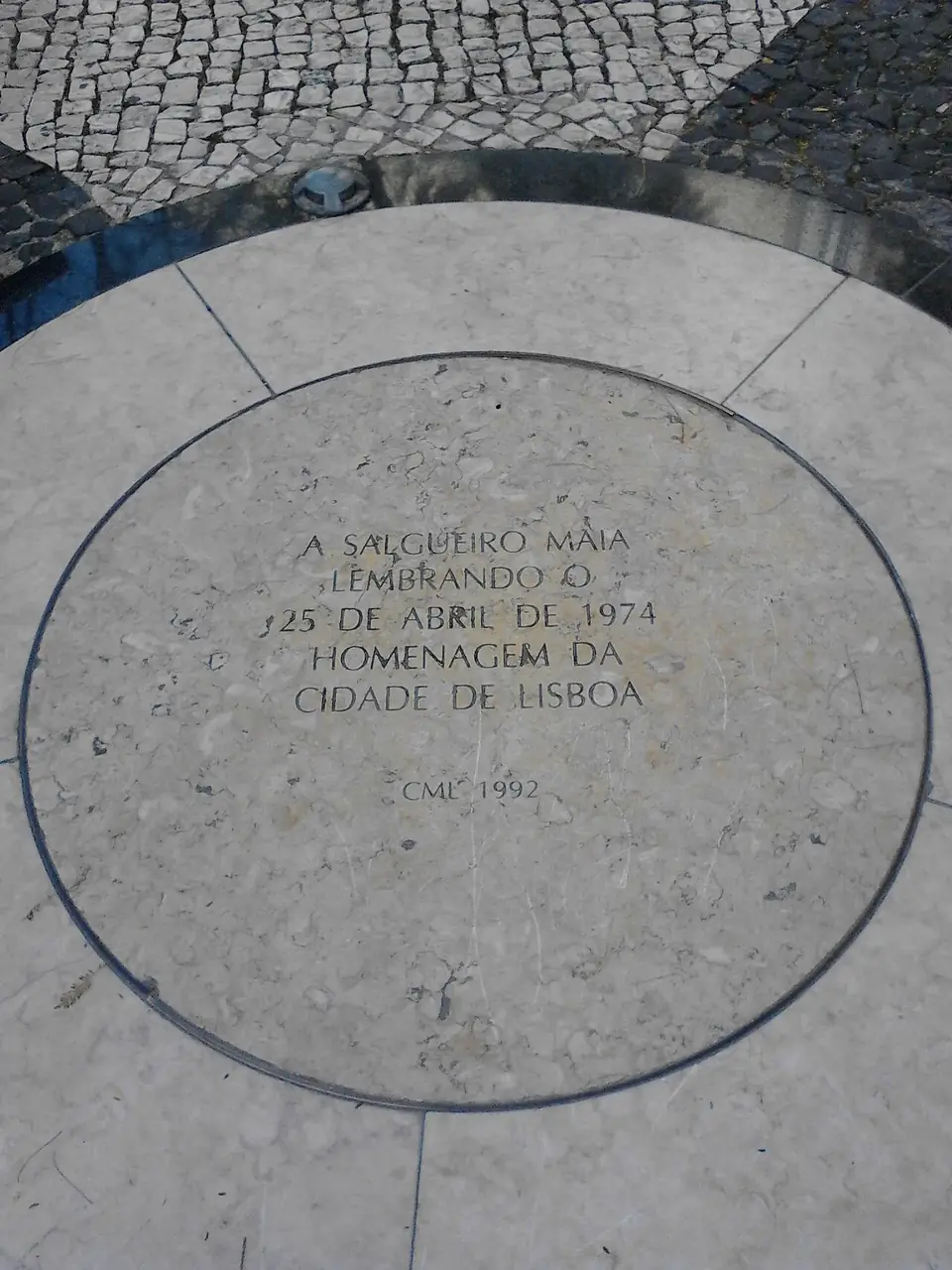 Círculo de pedra clara embutido na calçada portuguesa, com a inscrição «A Salgueiro Maia lembrando o 25 de Abril de 1974 – Homenagem da Cidade de Lisboa – CML 1992».