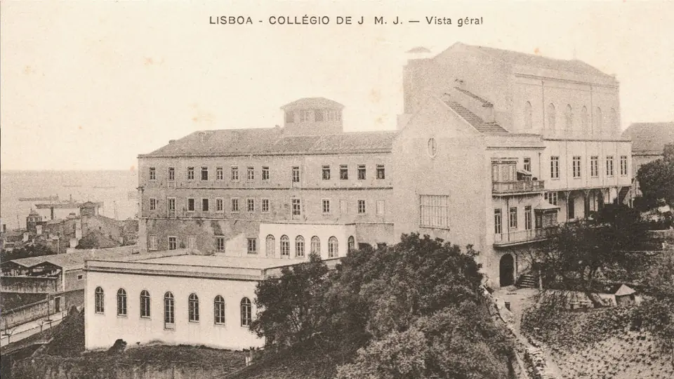 Postal antigo e amarelado com um grande edifício de muitas janelas no alto de uma encosta arborizada, sobre os telhados da cidade.