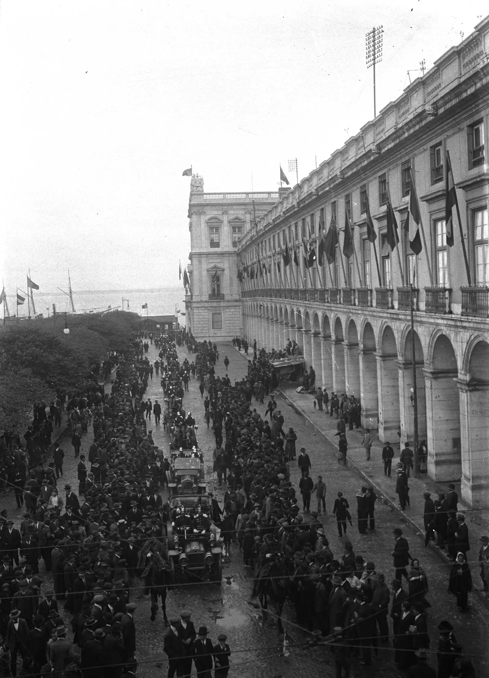 Fotografia a preto e branco: multidão compacta ao longo das arcadas da praça, vista do alto, com bandeiras penduradas nas janelas.