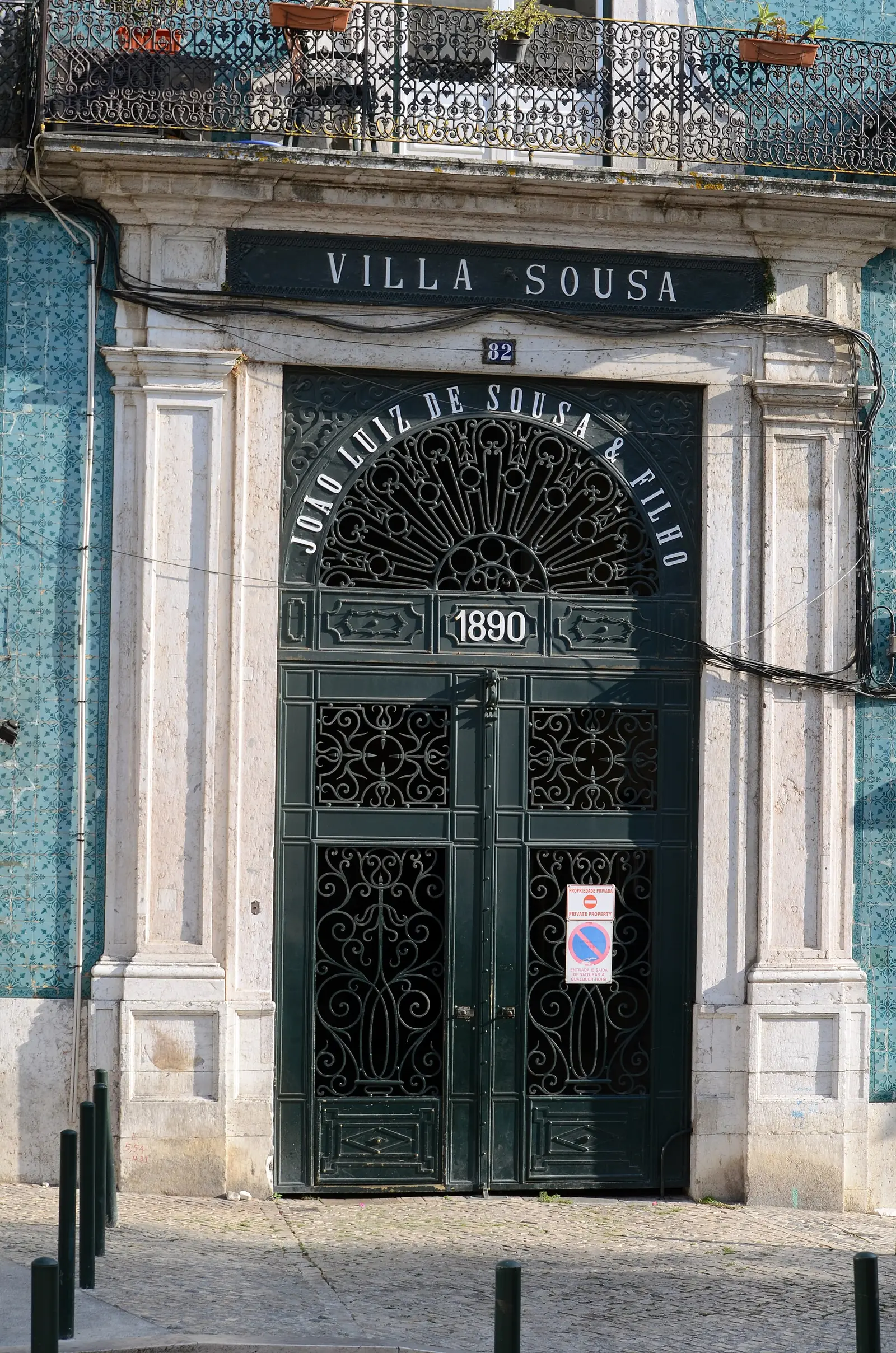 Portal de pedra clara com uma porta de ferro trabalhado, encimado pela inscrição «Villa Sousa» e pela data 1890, numa fachada de azulejos azuis.